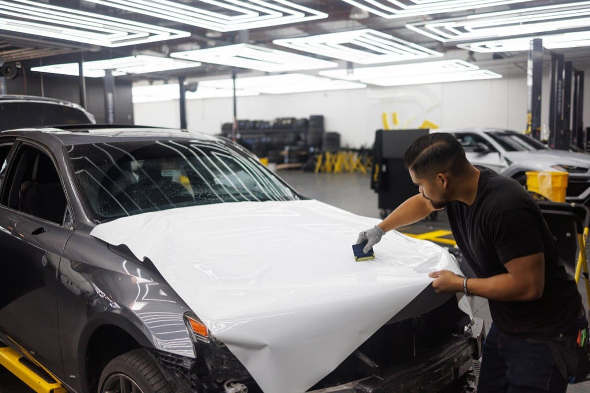A technician applying protective film to a car in a clean workshop