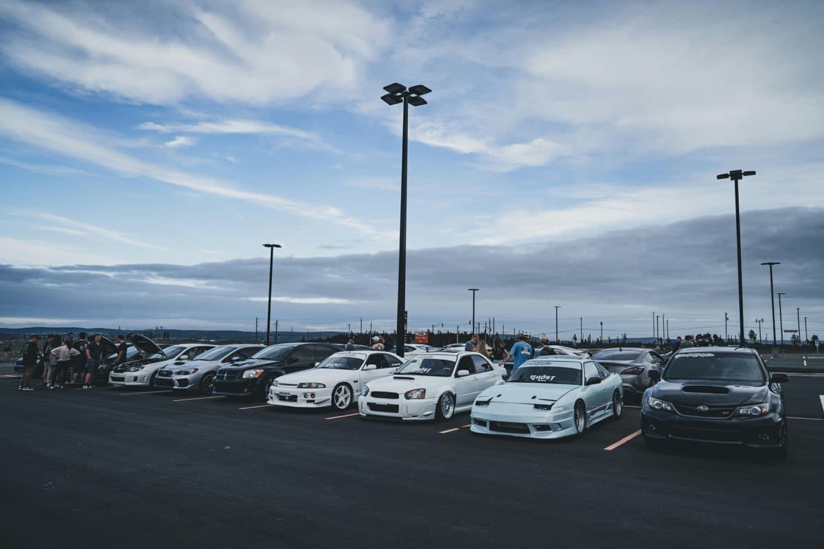 A line of modified cars at a club meet under a big sky